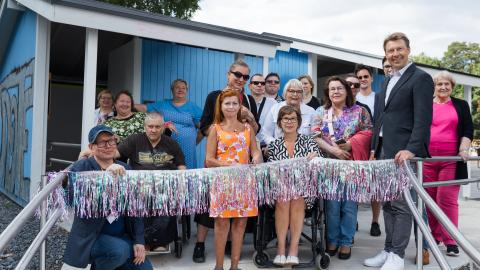 Ihmisiä Pyynikin esteettömän uimarannan avajaisissa. Oranssiasuinen vammaisneuvoston puheenjohtaja on leikkaamassa hopealamenauhaa.