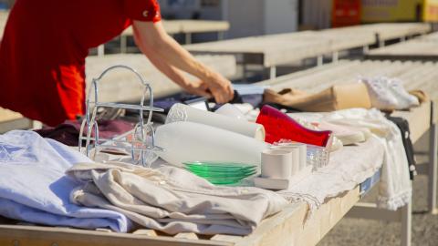 Nainen asettelee myytäviä tuotteita kirpputoripaikalle.