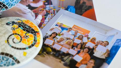 Kaksi valokuvaa pöydällä ihmisistä. Pöydällä on myös värikäs keramiikkatyö.