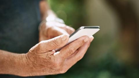 Vanhuksen kädet, jotka pitelevät älypuhelinta.