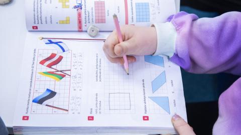 A hand of a pupil drawing to a school book.