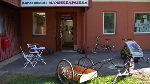 Different bicycles and a milk churn trolley at Kansalaistalo Mansikkapaikka&#039;s sunny front yard.