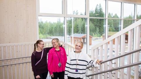 Kolme naista seisoo portaikossa rinnakkain. Taustalla ikkunoista näkyy metsä.