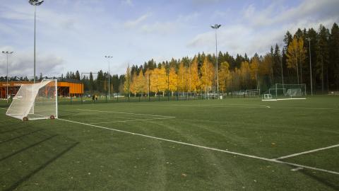 Jalkapallokenttä, taustalla rakennuksia ja metsää.