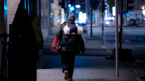 Nainen mustassa takissa ja mustissa housuissa kävelee jalkakäytävällä yöllä.