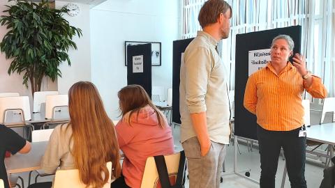 Kuvassa kaksi ihmistä keskustelemassa, opiskelijoita taustalla