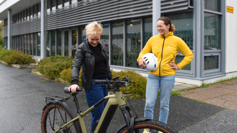 Kaksi henkilöä seisoo pyörän ympärillä pihassa.