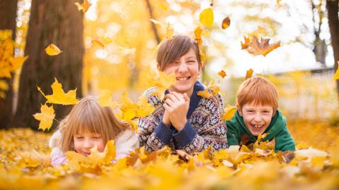 Kolme hymyilevää lasta syksyisten lehtien keskellä.