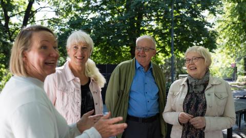 Neljä senioria keskustelee vilkkaasti ulkona Koskipuistossa.