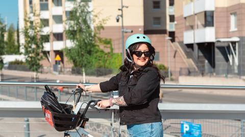 Pyöräilijä seisoo kaupunkipyörän selässä aurinkolasit ja kypärä päässä.