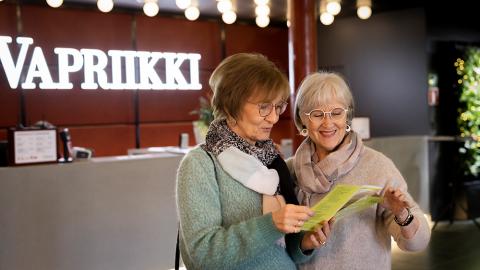 Kaksi eläkeläisnaista katselee Vapriikin esitettä museon aulassa. 