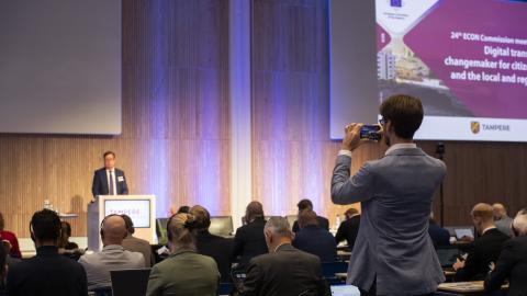 Mies ottamassa puhelimella kuvaa puhujasta konfrenssissa.