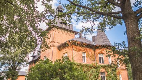 Suuri punatiilinen kartanorakennus pilkistää puiden lomasta.