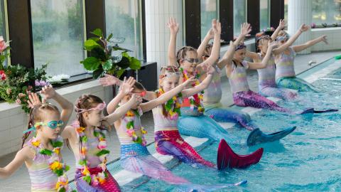 Tyttöjä uima-altaan reunalla vedenneitoasuissa.