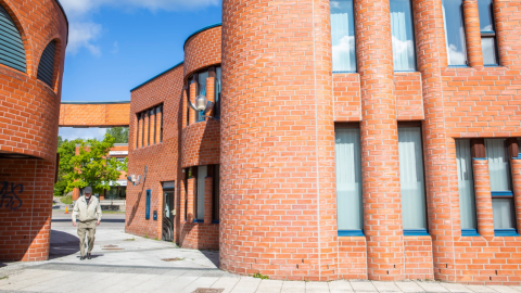 Reima ja Raili Pietilän suunnittelemia punatiilisiä rakennuksia Hervannan keskustassa. Talojen välissä kävelee hervantalainen.