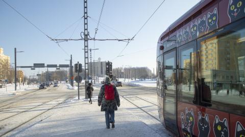 Ihmisiä ja kissakuvioinen raitiovaunu talviaikaan.