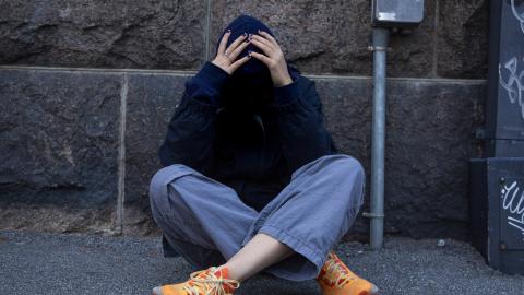 Nuori istuu maassa ja pitelee päätään käsissään.