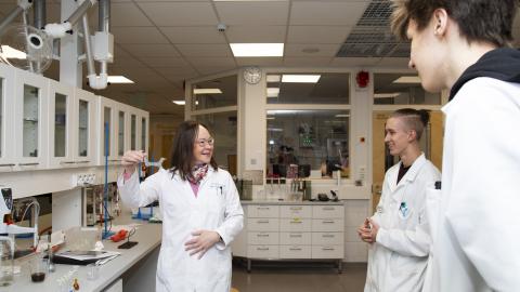 Kolme henkilöä seisoo laboratoriossa päällään valkoiset työtakit.