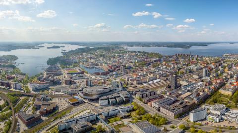 Tampereen kaupunkialue ilmasta käsin kuvattuna, etualalla tiivistä kaupunkia ja taustalla siintää järvimaisema.