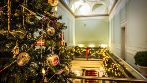 Joulukuusi on koristeltu runsaasti, taustalla näkyy lisää jouluvaloja kiinnitettynä yläkerran kaiteeseen.