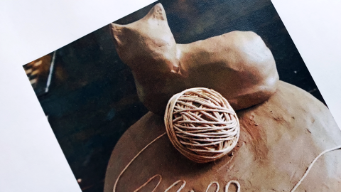 Savinen uurna, jonka päällä on kissa ja lankakerä.