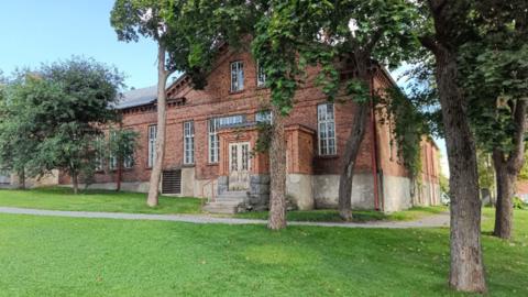 Vanha ja iso punatiilinen rakennus puiston keskellä.