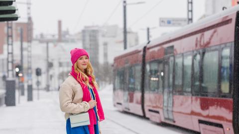 Punapipoinen tyttö odottaa ratikkaa talvisessa säässä ratikkaa.