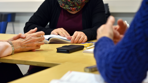 Three people’s hands on a table. There are study materials and a phone on the table.