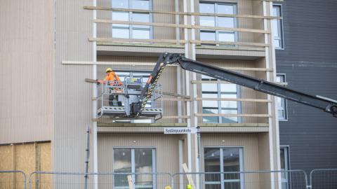 Rakenteilla olevan kerrostalon edustalla työntekijä nosturissa talon parvekkeen luona tekemässä työtään. 