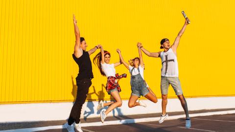 Kuvassa neljä henkilöä hyppäämässä ilmaan keltaisen seinän edessä