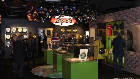 Vihreäsävyinen museosali, jossa esillä Manserock-näyttely. Näyttelyä katsomassa paljon ihmisiä.