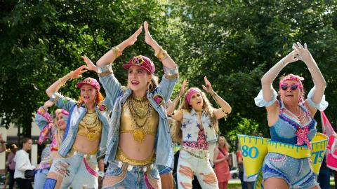 Värikkäästi pukeutuneita naisia tanssimassa kädet ylhäällä pään päällä.