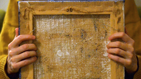 Ihminen pitää sylissään nurinpäin olevaa maalausta.