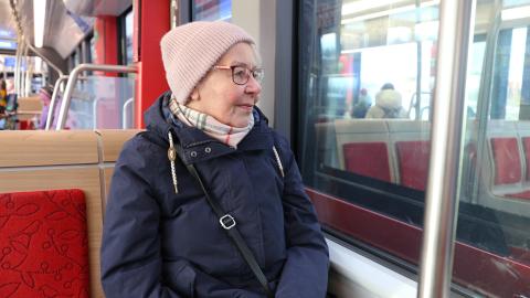 Vanhempi henkilö matkustaa ratikassa, katselee ulos.