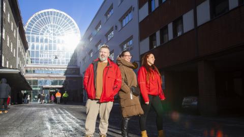 Kolme henkilöä kävelee aurinkoisena talvipäivänä Tullin alueella. Kahdella on päällään punainen ja yhdellä ruskea takki.