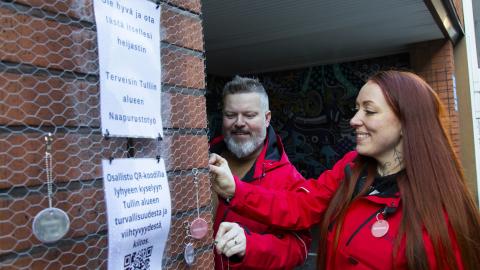 Tullintorin naapurustotyön punatakkiset työntekijät kiinnittävät Tullintorin ulkoseinään hankkeesta kertovaa heijastinta.