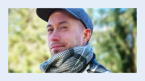 Henkilö katsoo viistosti kameraan. Taustalla näkyy vehreää maisemaa.