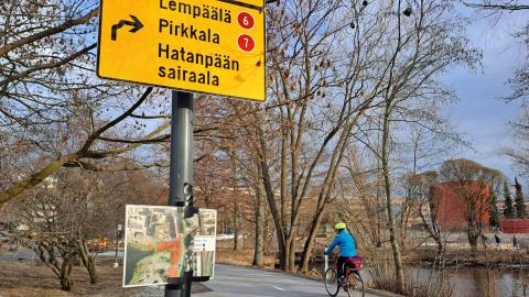 Etualalla pyöräilyn jatkuvuusopaste, taaempana pyöräilijä pyörätiellä.