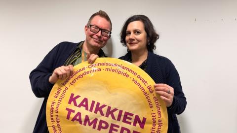 Yhdenvertaisuusvaltuutettu Mikko Ala-Kapee ja projektisuunnittelija Ilaria Tucci pitävät käsissään suurta keltaista kiekkoa, jossa lukee Kaikkien Tampere.