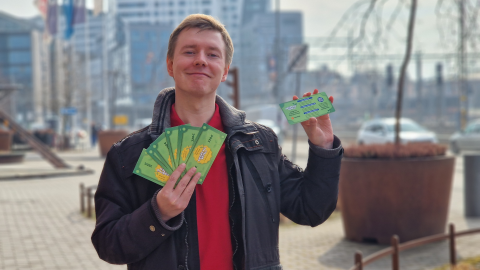 Henkilö seisoo pihalla ja esittelee kameralle vihreää Kesätyöseteliä. Taustalla näkyy korkeita kerrostaloja.