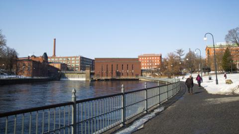 Tammerkosken rannan tuntumassa Koskipuistossa menee kävelytie ja taustalla näkyy voimalaitoksen punatiilisiä rakennuksia.