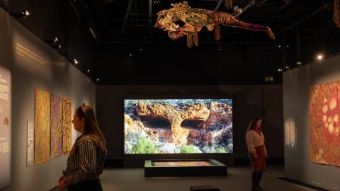 Kaksi ihmistä hämärässä näyttelytilassa katselee seinällä olevia maalauksia.