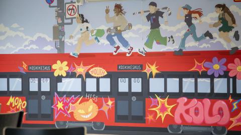 Seinä, jossa muraali, jossa punainen ratikka, jonka katolla juoksee nuoria