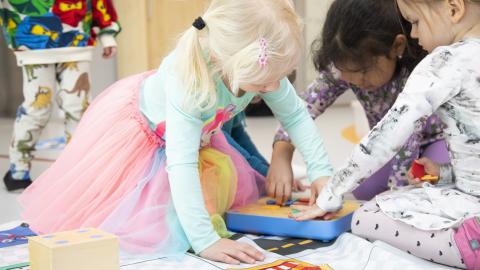 Kolme pientä tyttöä leikkii lattialla.