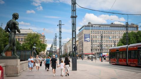 Ihmisiä kävelee Hämeensiltaa pitkin kesäpäivänä, vieressä ajaa ratikka.