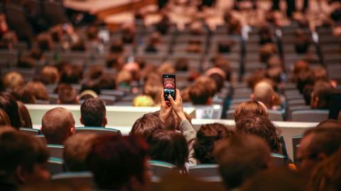 Katsojia Tampere-talon salissa ennen Tampere Filharmonian konsertin alkua. Yksi katsojista kuvaa etualalla näkyvää orkesteria kännykällä.