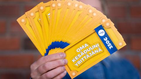 Henkilön ojennetussa kädessä on viuhkan muotoisena nippu seteleitä, joissa lukee Oma kesäduuni yrittäjänä sekä summa 350 euroa. Seteliviuhka peittää henkilön kasvot. 