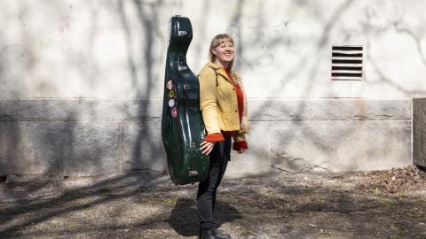 Kielo-Kristiina Kärkkäinen seisoo ulkona sellokotelo selässään.