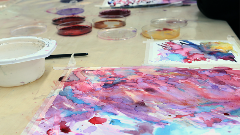 Kuvataidetyö ja luonnonväripurkkeja pöydällä.