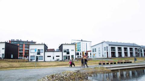 Ihmisiä kävelemässä lammen rannalla asuinalueella.